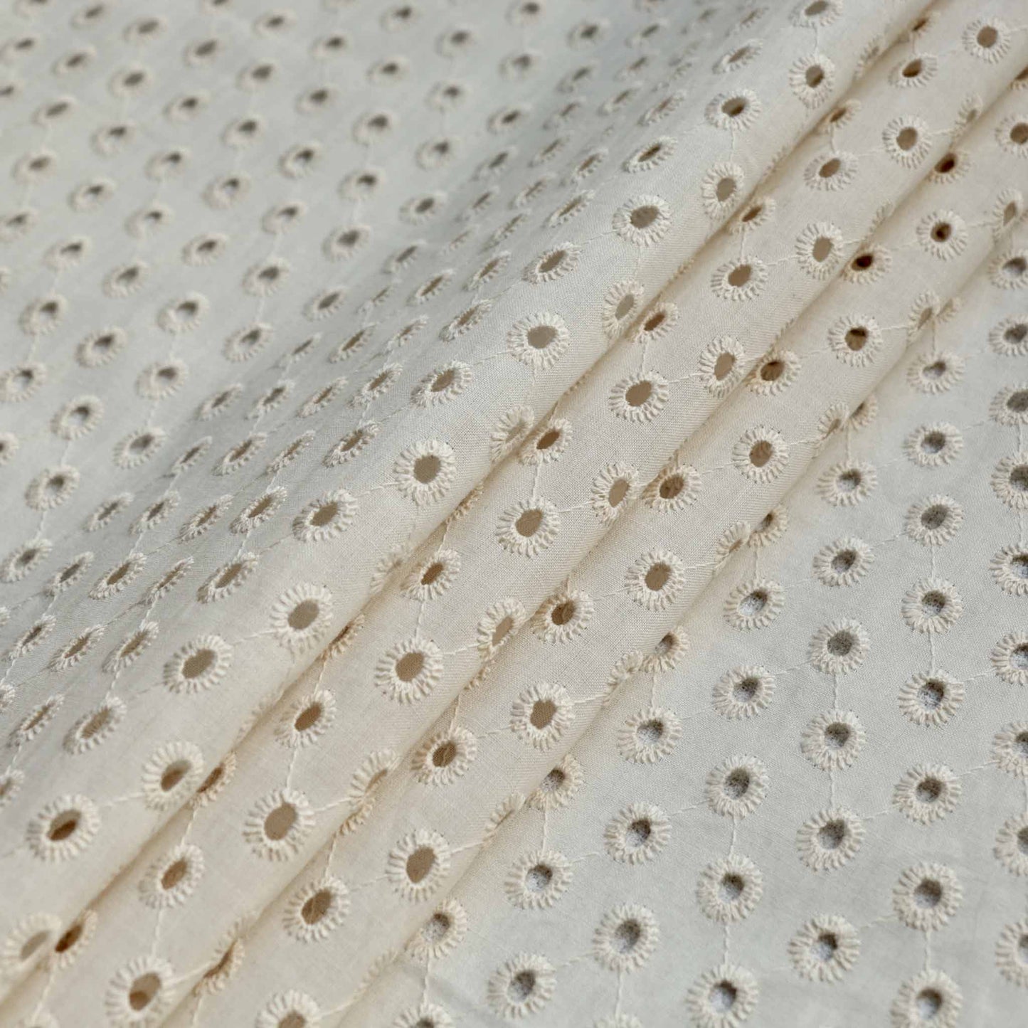 folded ivory broad anglaise dressmaking fabric with single hole embroidery design