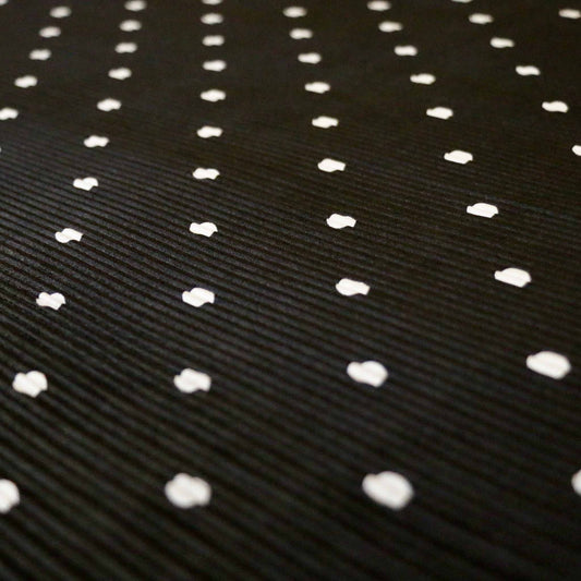 black stretchy plisse dressmaking fabric with white polka dot pattern